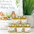 Jars of honey with personalized labels for a birthday party on a white surface.