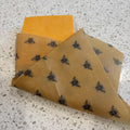 Beeswax wrap with bee pattern wrapped around block of cheese on speckled white background