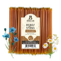 Pack of honey sticks with a label on a white background, surrounded by flowers.