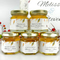  Small honey jars with personalized labels in front of blurred background