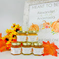 Jars of honey with personalized labels in front of a decorative sign with pumpkins and flowers.