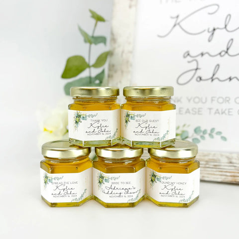 Five jars of honey with personalized labels on a white surface.