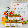 Jars of honey with personalized labels in front of a framed decorative sign. 