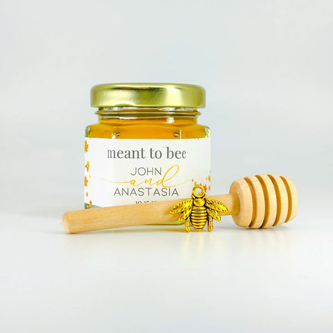 Jar of honey with a gold lid, gold bee charm, and wooden dipper on a white background