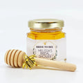 Jar of honey with a gold lid, gold bee charm, and wooden dipper on a white background, featuring 'Bride to Bee' Melissa's Bridal Shower text.