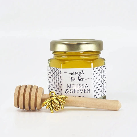 Jar of honey with a gold lid, gold bee charm, and wooden honey dipper on a white background
