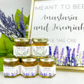 Jars of honey with personalized labels in front of a sign with 'Meant to Bee' text, surrounded by lavender flowers.