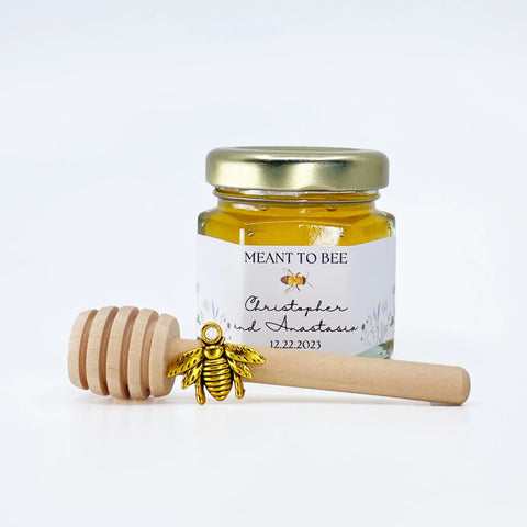 Jar of honey with a gold lid, gold bee charm, and wooden honey dipper on a white background