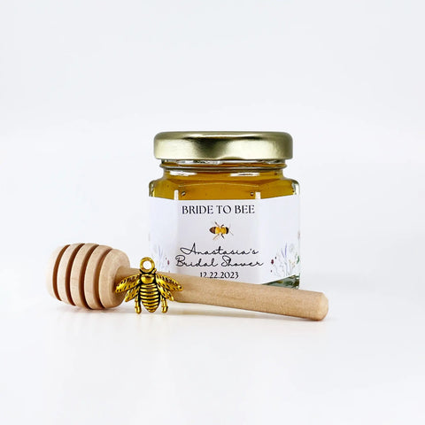 Jar of honey with a gold lid and wooden honey dipper on a white background, featuring 'Bride to Bee' branding.