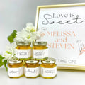 Honey jars with personalized labels in front of a 'Love is Sweet' sign.