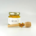Jar of honey with a wooden dipper and honeycomb charm on a white background