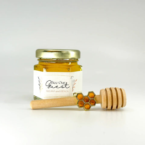Jar of honey with a wooden dipper and honeycomb charm on a white background