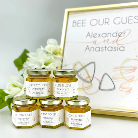 Jars of honey with personalized labels in front of a decorative sign.