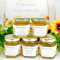 Jars of honey with personalized labels on a white surface with sunflowers in the background.