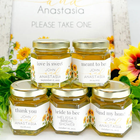 Jars of honey with personalized labels on a white surface with sunflowers in the background.