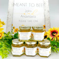 Jars of honey with personalized labels surrounded by flowers and a sign reading 'Meant to Bee'.
