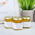Three jars of honey with personalized labels on a white surface with a plant in the background.